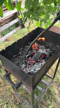 A person uses a stick to adjust red-hot coals in a barbecue grill outdoors. High quality 4k footage