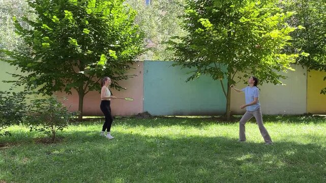 Two happy young women playing badminton outdoors in backyard