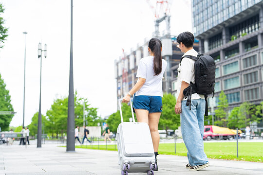 街を歩く観光客カップルの後ろ姿。旅行、観光、インバウンド、外国人、歩行者、荷物、日本、都会、ツアー