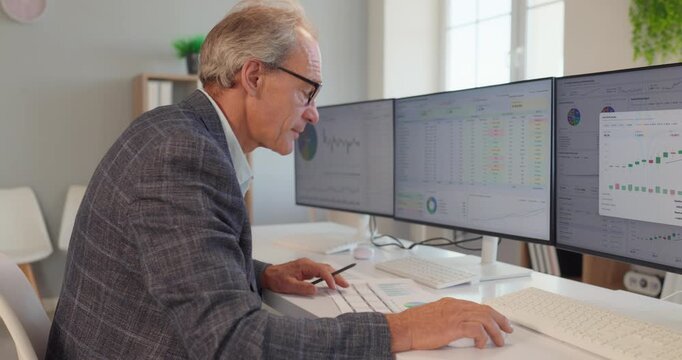 Mature investment analyst works on three monitors. He works with risk tables and allocation charts. The office is bright and modern. Concept of investment portfolio and risk management.