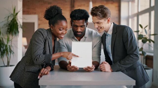 Pointing woman in checked blazer guiding review after center man presenting spiral pad in loft