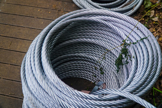 Coiled Silver Steel Wire Rope on Wooden Deck with Green Vine