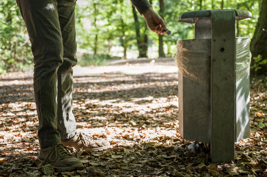 A person throws trash into a public trash can in a public park