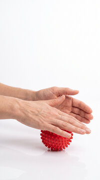 Adult hand pressing a red spiky massage ball against a smooth white surface, hand therapy, sensory stimulation, rehabilitation exercise, trigger point massage, physiotherapy equipment, fine motor trai