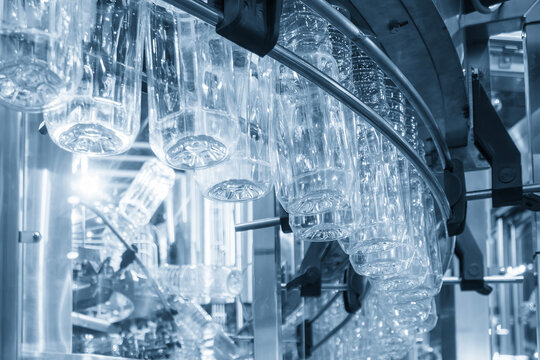Close up of PET bottles hanging on an overhead conveyor belt during a drinking water filling process in a blue tone scene