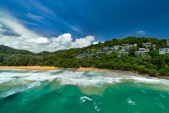 Picturesque tropical coastline featuring buildings amidst jungle vegetation and a golden sand beach with heavy surf and dangerous rip currents, swimming is prohibited.