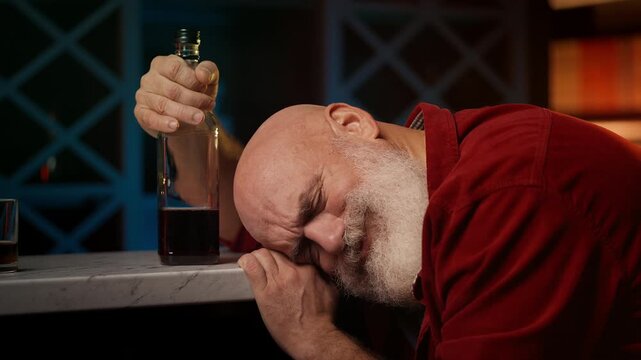 Lonely middle-aged man asleep at bar counter by whiskey bottle, depression