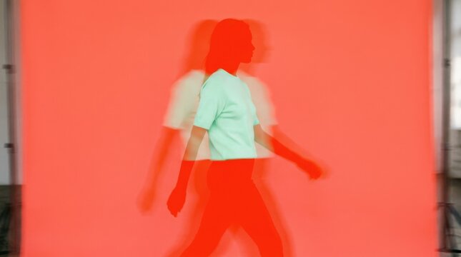 Bright red-orange human silhouette on a saturated coral background wearing a pale mint top, body vibrating through repeated lateral exposures, minimalist fashion photography with intense complementary