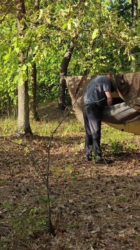 A camper organizes gear under a hanging tarp in the forest.