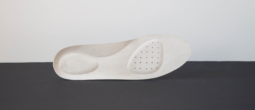 White leather orthopedic insole for footwear comfort isolated on minimalist black and white geometric background. Prevention and treatment of flat feet. Foot care