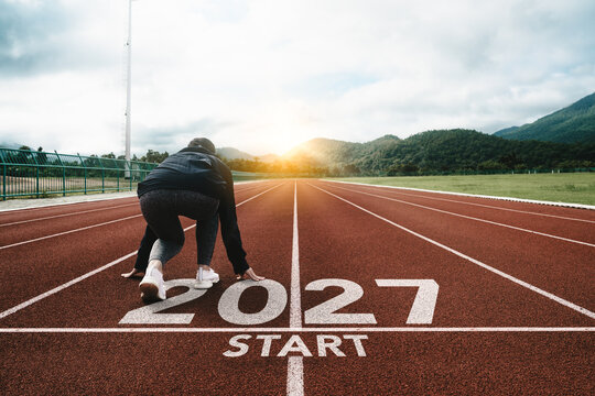 New year resolution 2027 concept. Word start 2027 on athletics track and athlete woman runner preparing to new year at sunset for challenge and beginning planning health and the goal to success.