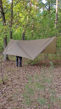 Male camper steps under a pitched tarp shelter in the woods.