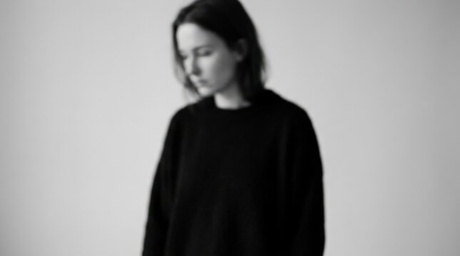 Anonymous person rendered intentionally out of focus against a light gray background, conceptual portrait photography, black clothing, soft motion blur, minimal monochrome palette and modern themes of