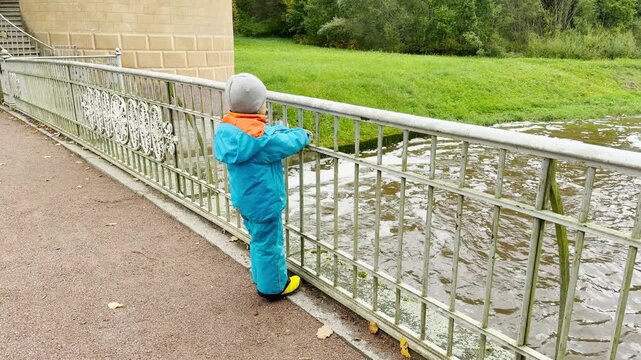 A curious child looks at the river from the Pil-Tower Bridge in Pavlovsk Park, Saint Petersburg. This peaceful moment brings a sweet feeling of wonder and joy.