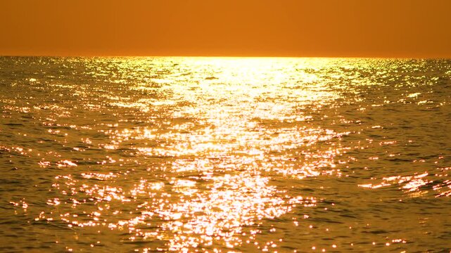 Golden sunlight glimmers upon dark rolling sea waves during a tranquil summer twilight. Static tripod shot.