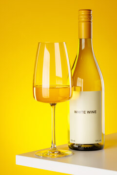 White wine bottle and glass on yellow background elegant drink setup