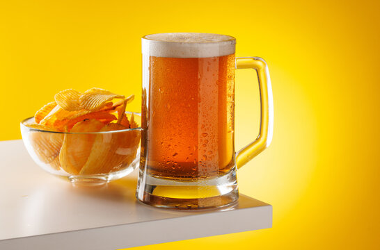 Beer mug with foam and chips on yellow background snack setup