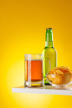 Beer mug with foam chips and bottle on yellow background snack setup
