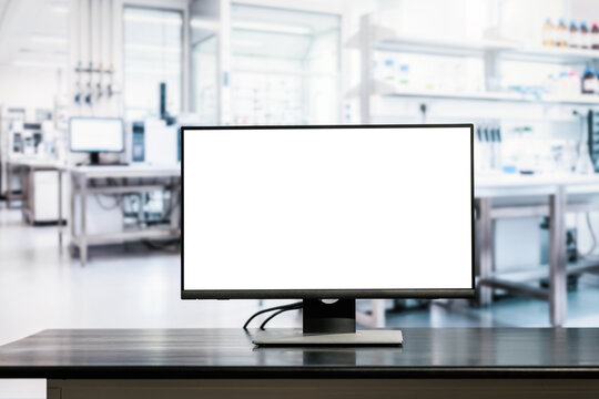 Blank desktop computer monitor on a dark table in a bright modern laboratory, with blurred scientific equipment and workspace in the background.