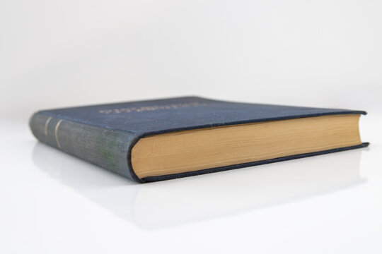 Thick hardcover book on a white reflective surface, side angle.