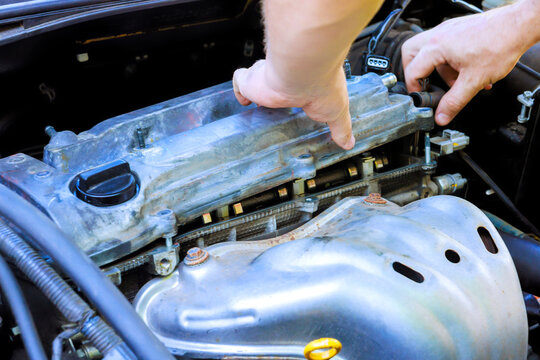 Worker works on valve cover of car engine in a garage tools, parts are nearby as maintenance happens.