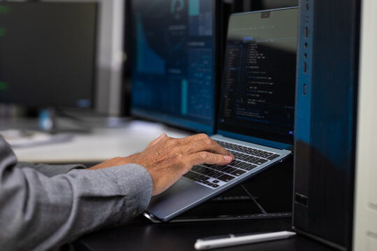 Close-up of a person typing code on a laptop beside server racks in a modern data center, cybersecurity, software development, and network management.