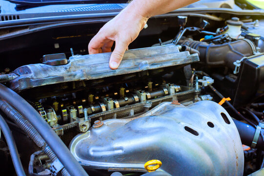 Mechanic is removing valve cover from car engine inside garage tools, car parts are visible.