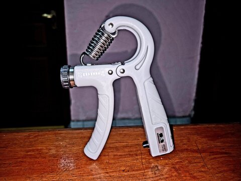 Adjustable hand grip strengthener with a rest and a rep counter, resting on a wooden table.