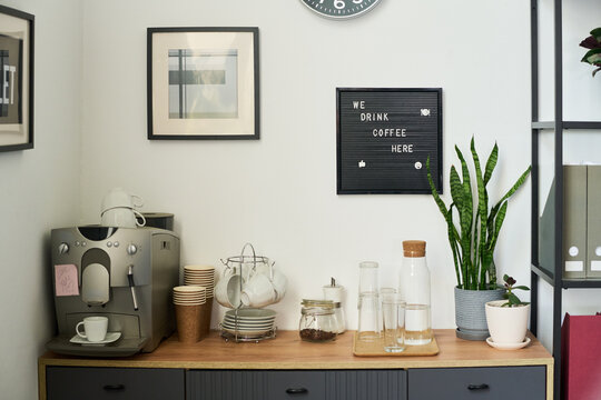 Espresso maker, cups, glassware arranged on cabinet in office breakroom area. Perfect for workplace culture, corporate wellness, employee perks marketing materials