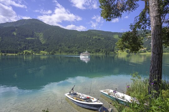 Small rowing boats and boat of the Wei&szlig;enseeschifffahrt arrives at the landing stage at Ronacherfelsen, Wei&szlig;ensee, Carinthia, Austria