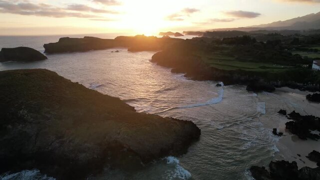 Aerial view of Barro Beach at sunrise with waves washing over a rocky sea stack, Llanes, Asturias, Spain