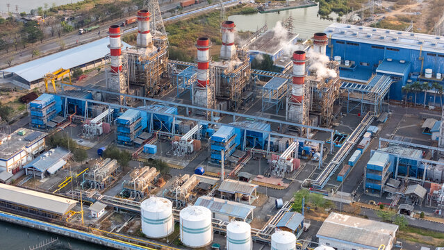 Aerial view of an industrial power plant with tall chimneys emitting smoke, complex piping, blue buildings, and large storage tanks in Semarang, Central Java, Indonesia.