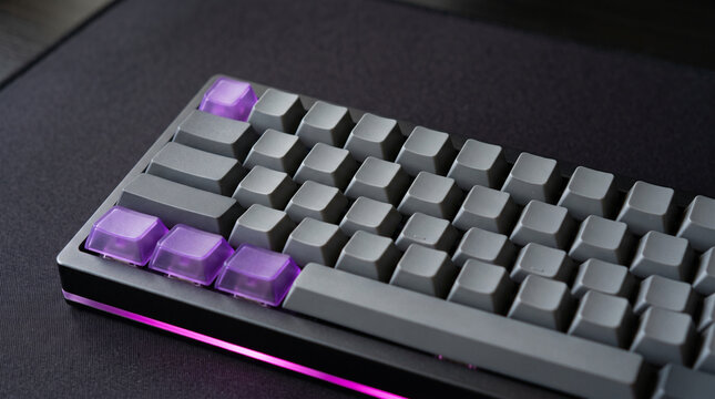 Modern mechanical computer keyboard with custom purple keycaps and dark deskmat background.