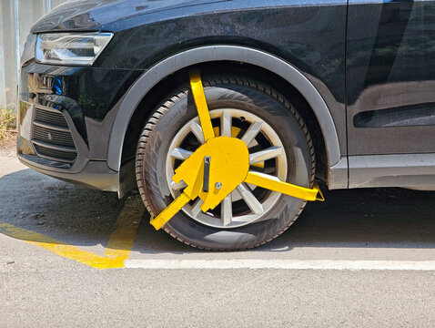 Yellow wheel clamp locked on parked car tire for traffic violation and illegal parking penalty on street
