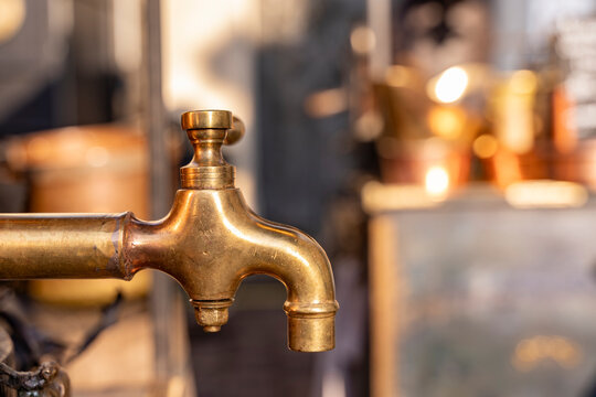 Vintage brass faucet connecting to industrial brewing equipment in distillery with bokeh background
