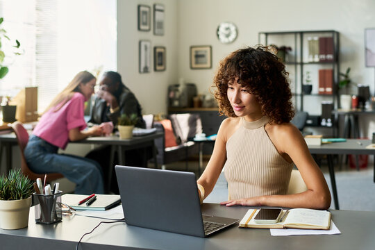 Young multi-ethnic woman graphic designer working on laptop in modern creative studio. Multiethnic team collaborating in background, suitable for corporate branding and technology marketing