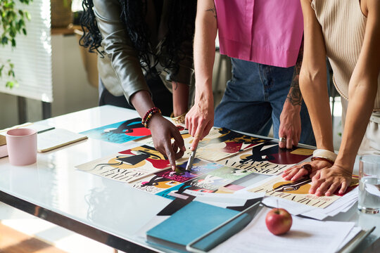 Diverse group of young adult women designers reviewing branding posters on desk in creative agency studio. Concept illustrates collaborative graphic design workflow for business marketing