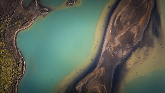 Aerial view of turquoise glacial water and intricate brown sand sediment patterns in the landscape of Vik, Myrdalshreppur, Iceland.