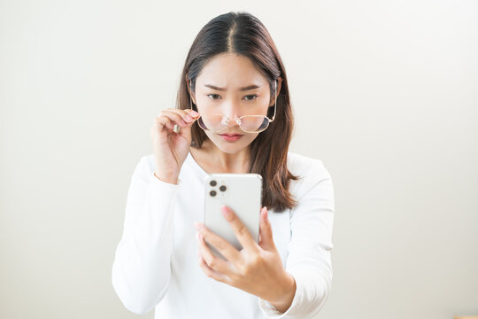 Presbyopia, Hyperopia middle aged asian woman holding eyeglasses problem with vision blurred ,trying to read text message from smart mobile phone screen, eye disease of old, eyesight farsightedness.