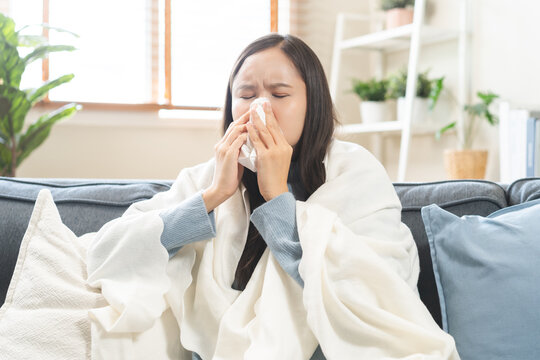 Sick, coronavirus or covid, tired asian young woman have a fever, flu and hand in use tissues paper sneezing nose, runny while sitting on sofa, couch at home. Health care with disease, pandemic virus