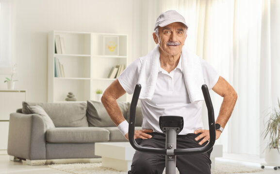 Elderly man with a towel around his neck on a stationary exercise bike at home