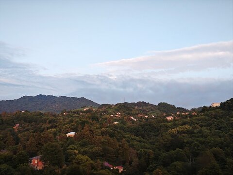 Landscape photograph of rolling hills covered in dense green forest. Scattered houses on a hillside during golden hour