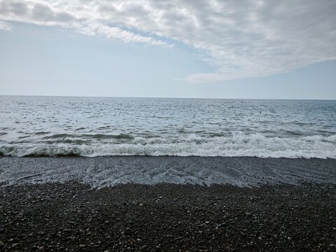 Small wave breaking on a pebble beach. Gentle sea and cloudy sky over the rocky coastline