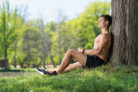 Athlete man resting against a tree