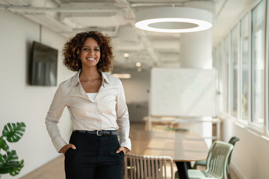 Smiling latin business woman standing for portrait in coworking office meeting room, looking at camera. In 30s, female analyst works as advisor, agent, banker, broker, accountant. Copy space