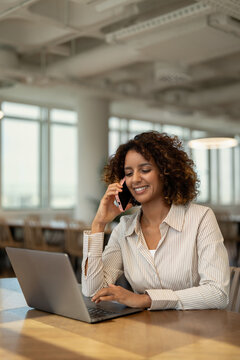 Vertical portrait of american business woman talking on mobile phone in coworking office workspace, having client call. In 30s, female worker works as professional, businesswoman, manager, executive