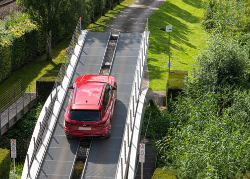 Wolfsburg, Germany - 15 Jul 2024: Red Volkswagen crossover vehicle navigating an inclined metal ramp on an obstacle test course at Autostadt park