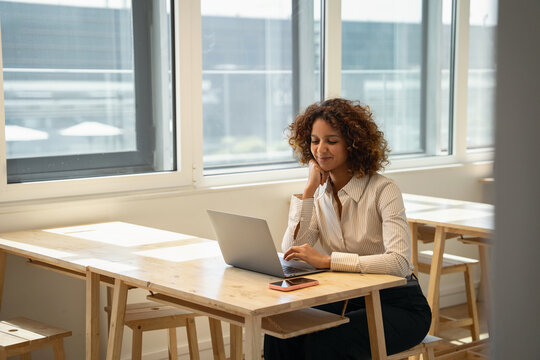 Smiling indian business woman thinking at laptop computer in coworking office workspace, working online. In 30s, female director works as founder, analyst, advisor, agent, banker. Copy space