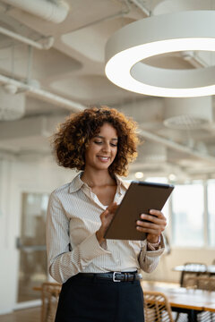 Vertical portrait of multiracial business woman browsing on digital tablet in coworking office workplace, using touchscreen. In 30s, female staff works as worker, professional, businesswoman