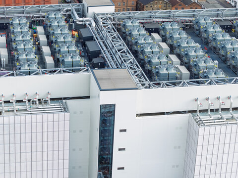 Aerial view of a modern data center rooftop featuring rows of industrial cooling units, complex ventilation systems, and metallic piping on a white building structure in the United Kingdom.